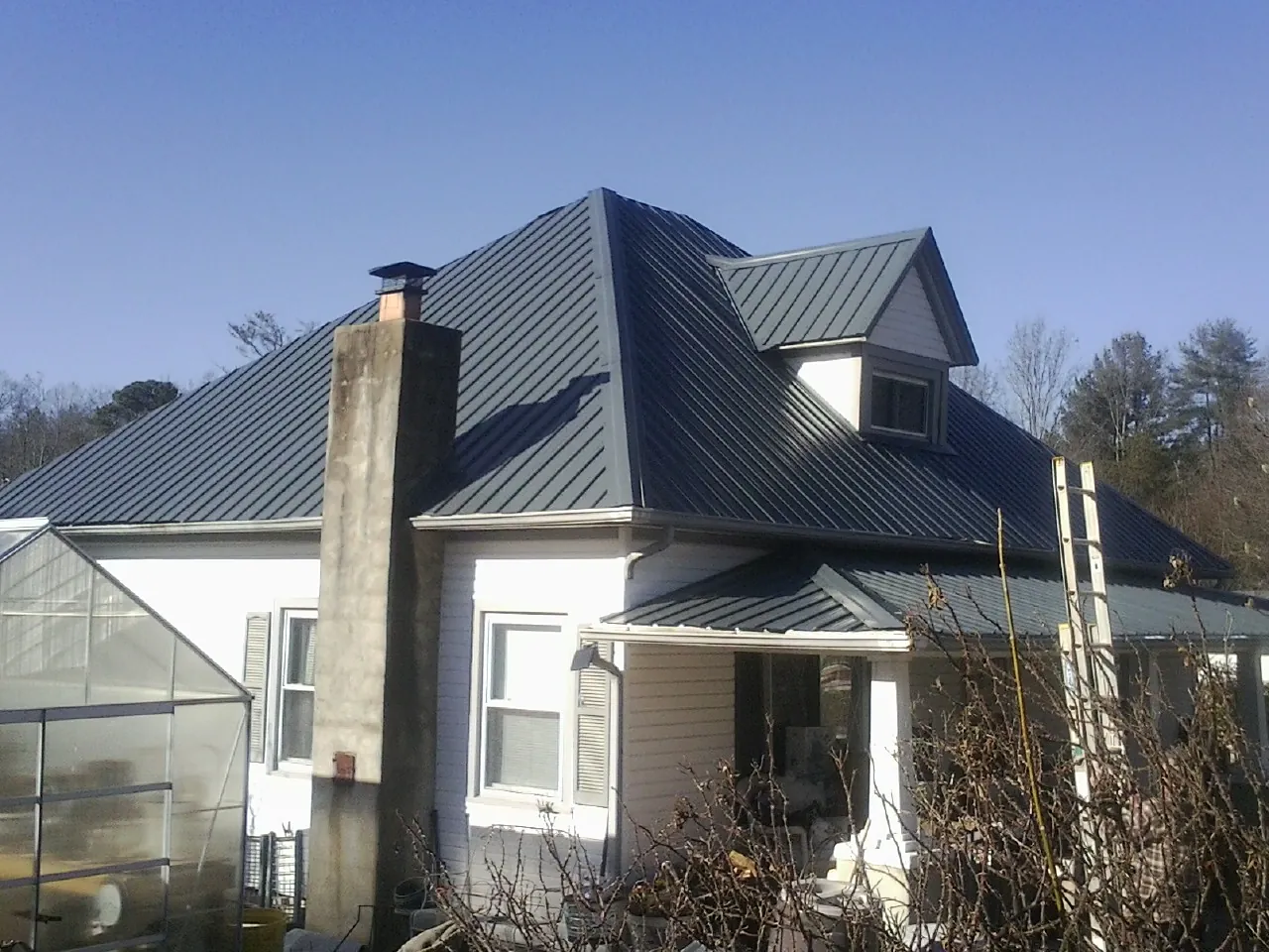 Dark blue standing seam metal roof on a white farmhouse with dormer — Slate & Tile Roof Repair by Roofing Brothers in Currituck