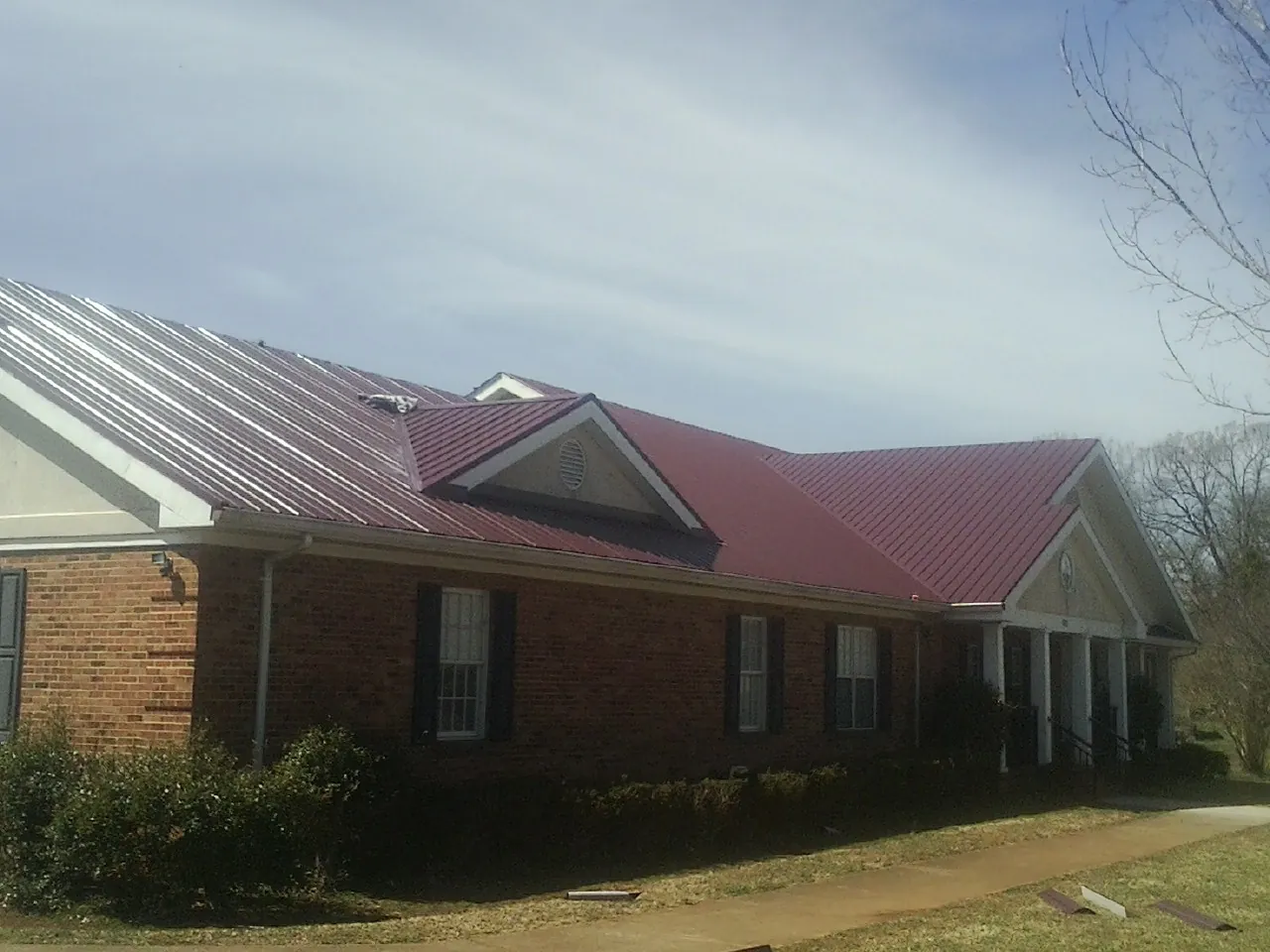 Red metal roof with gabled entries on a long brick building, from a Hail Damage Roof Repair job in Currituck