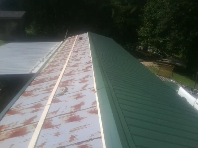Old rusted panels beside newly installed green metal roofing — Wind Damage Roof Repair by Roofing Brothers in Currituck