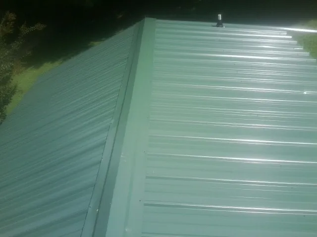New green metal panels meeting at the ridge of a roof — Flat Roof Repair work by our crew in Currituck