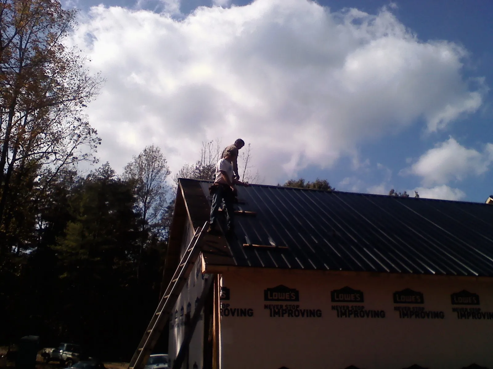 Roofer fastening dark metal panels high against a cloudy sky, from a Roof Inspection job in Currituck