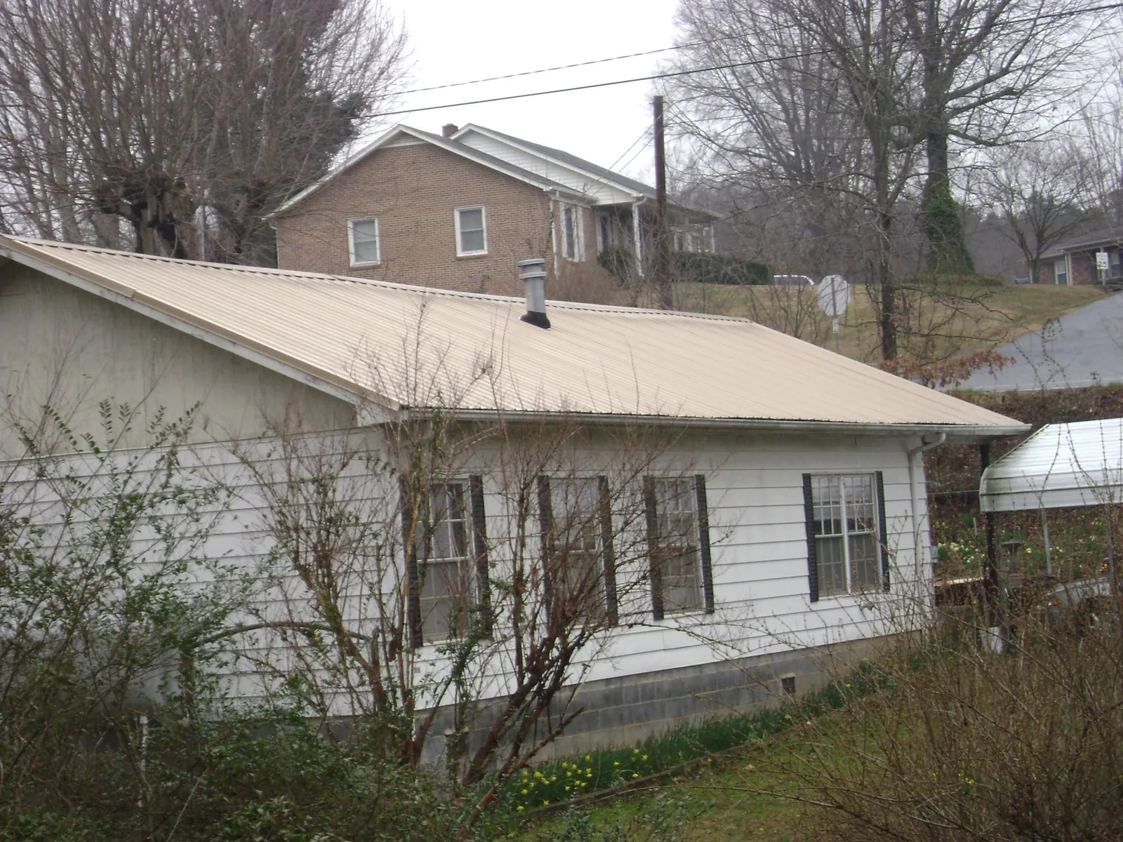 Tan metal roof on a white sided house set into a hillside — Commercial Roofing by Roofing Brothers in Currituck